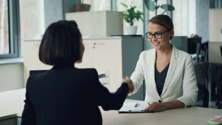 Two women shaking hands across a desk