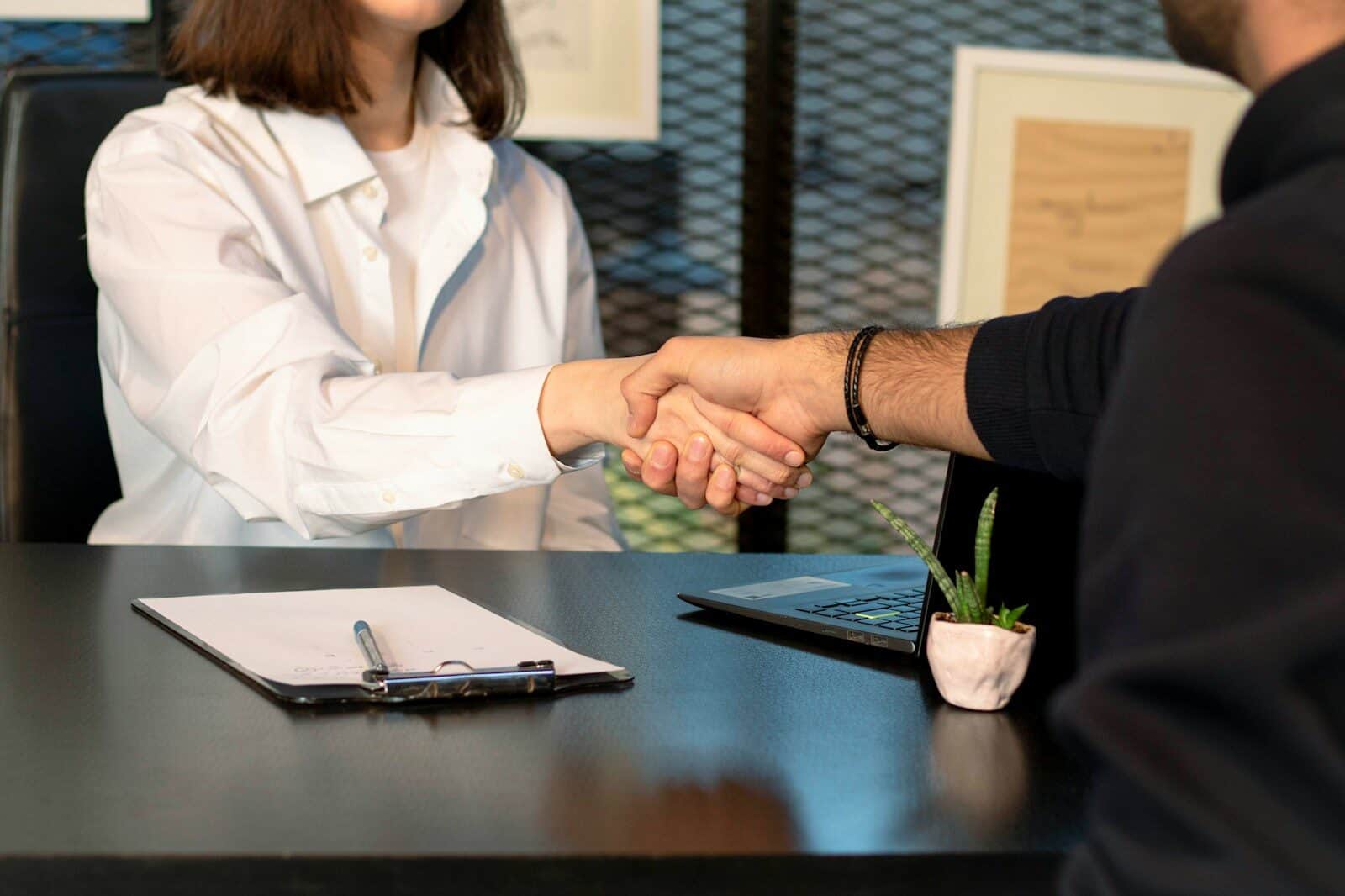 Ein Mann und eine Frau, die sich vor einem Laptop die Hand geben